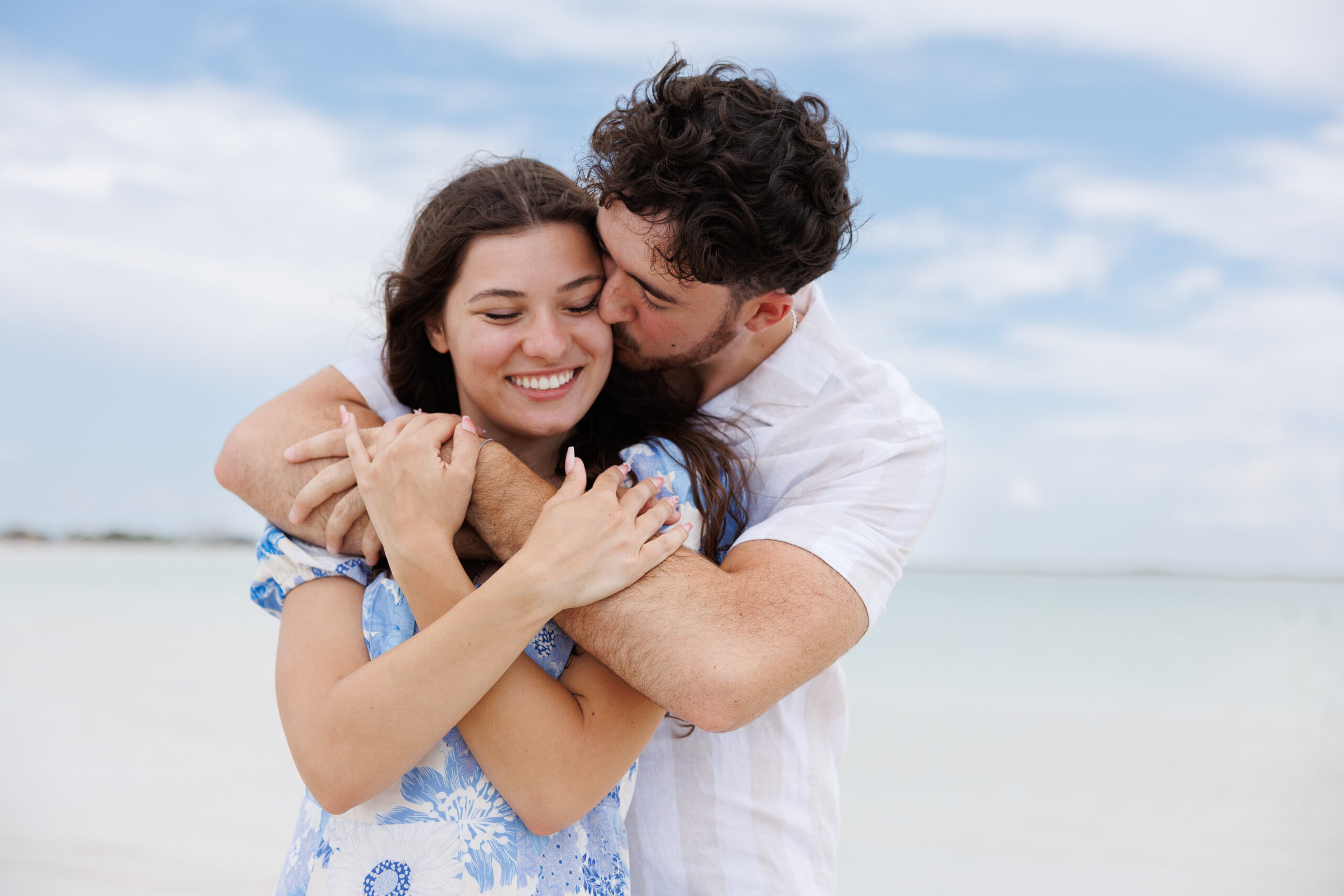 7N4A8742 A close-up of a bride and groom holding hands, showcasing their wedding bands and elegant attire against a softly lit background.