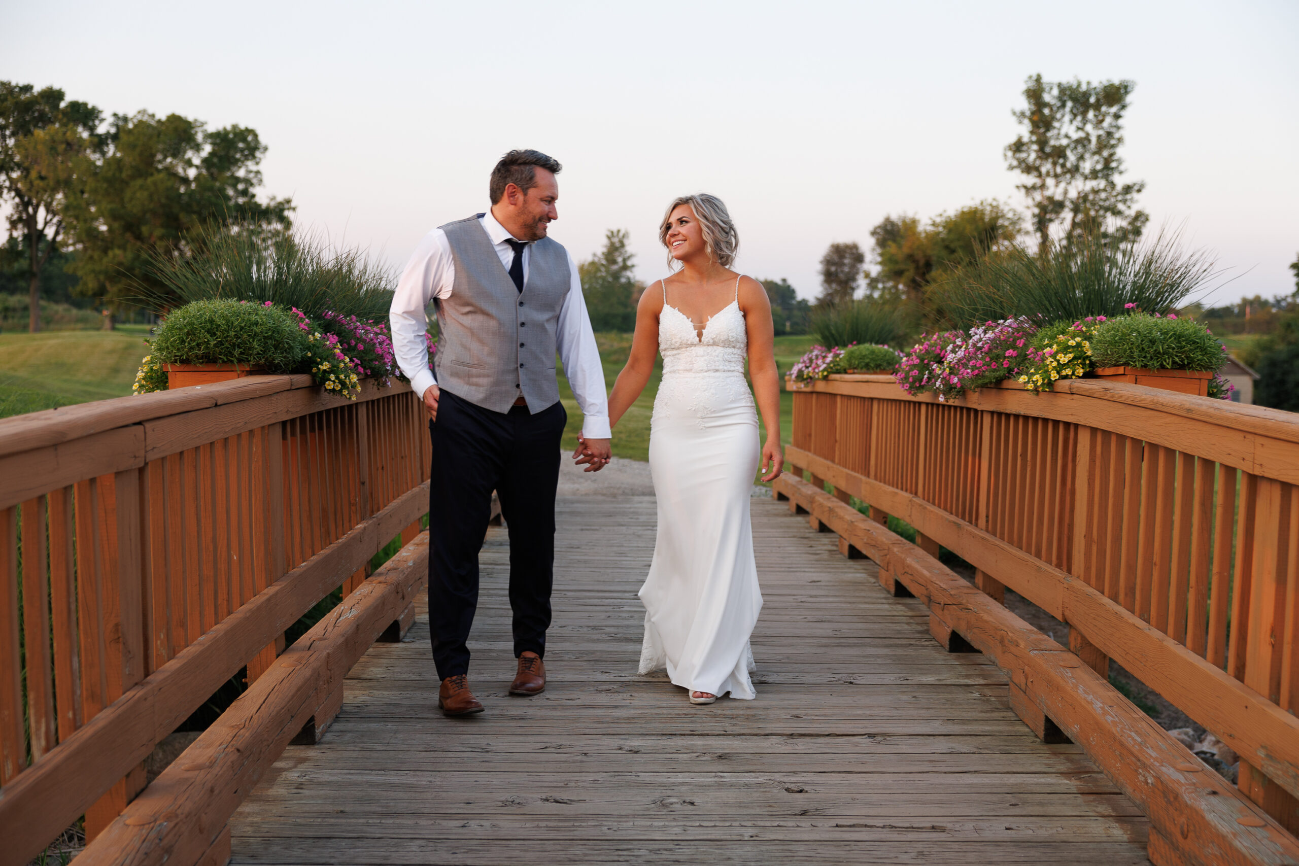 LO1A7183 A close-up of a bride and groom holding hands, showcasing their wedding bands and elegant attire against a softly lit background.